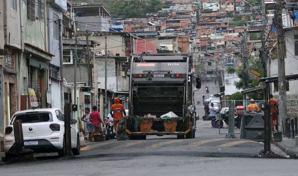 Caminhão de lixo cruza barricadas para acessar a Vila Cruzeiro; na semana passada, um carro queimado ocupava o local — Foto: Fabiano Rocha / Agência O Globo