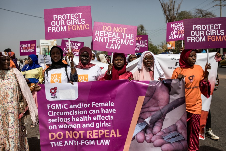 Manifestantes contra a mutila&ccedil;&atilde;o genital feminina (MGF) seguram cartazes do lado de fora da Assembleia Nacional, em Banjul