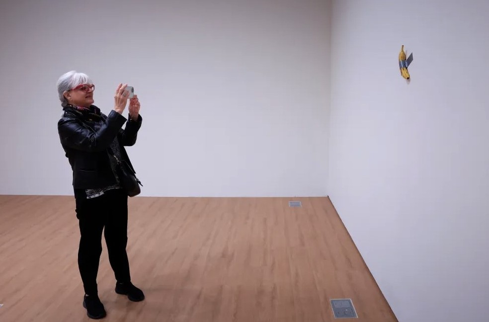 Visitante de museu francês fotografa a obra com banana e fita adesiva do italiano Cattelan — Foto: AFP