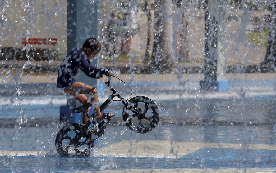 Inverno de calor recorde. No Parque de Madureira, um garoto anda de bicicleta embaixo d'água