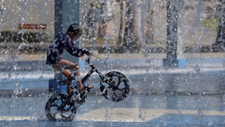 Inverno de calor recorde. No Parque de Madureira, um garoto anda de bicicleta embaixo d'água — Foto: Fabiano Rocha