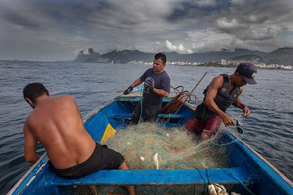 Carlos Eduardo da Costa, de 40 anos, conhecido como Pixico, à direita, observando o peixe na rede — Foto: André Arruda/Agência O Globo