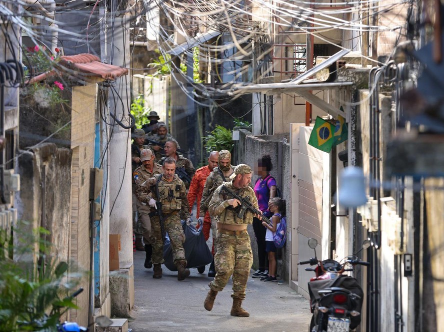 Mulher cobre o rosto de criança durante a passagem de policiais com o corpo de suspeito morto em operação na Ladeira dos Tabajaras