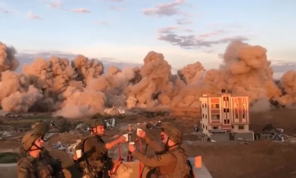 Relaxados, soldados israelenses erguem copos com explos&otilde;es em pr&eacute;dios na Faixa de Gaza ao fundo &mdash; Foto: Reprodu&ccedil;&atilde;o/Facebook