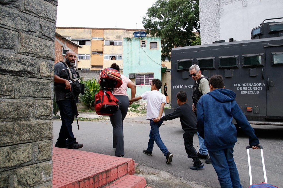 Estudantes passam por policiais armados e veículo blindado na Favela do Muquiço — Foto: Marina Calderon / Agência O Globo