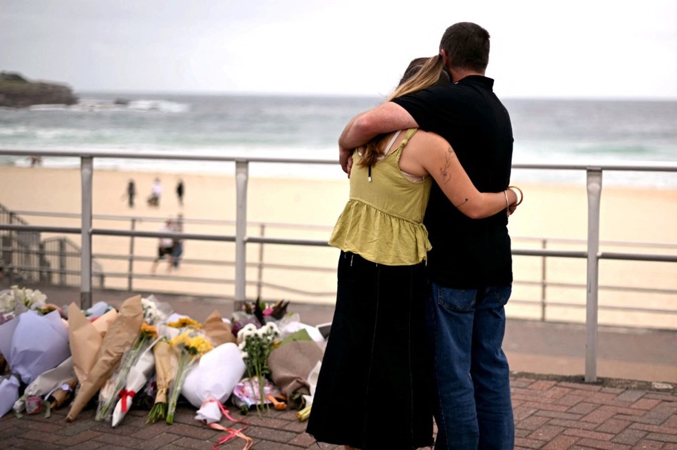 Casal de abra&ccedil;a em Bondi Beach diante de homenagens aos 15 mortos no massacre em Sydney &mdash; Foto: AFP