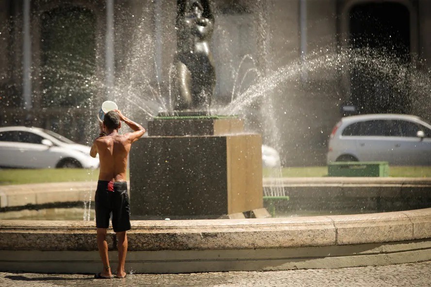 Homem usa água do chafariz para se refrescar no centro do Rio de Janeiro