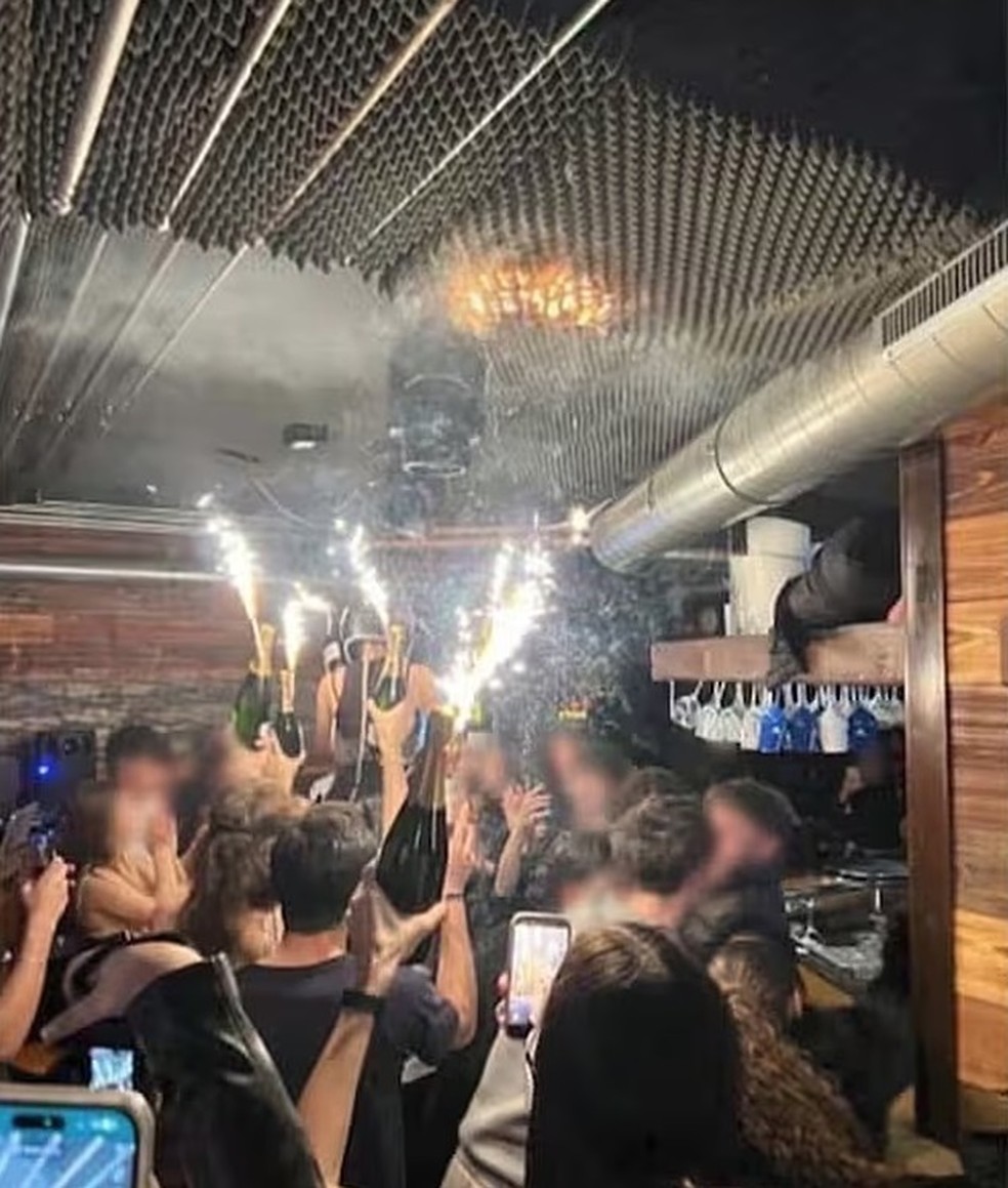 Chamas se iniciam no teto do Constellation enquanto garçonete e clientes seguram garrafas de champanhe com vela pirotécnicas — Foto: Reprodução