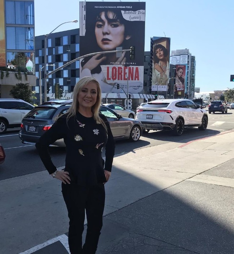 Lorena Bobbitt na frente de cartaz com propaganda sobre o caso em que decepou o pênis do marido — Foto: Reprodução/Instagram