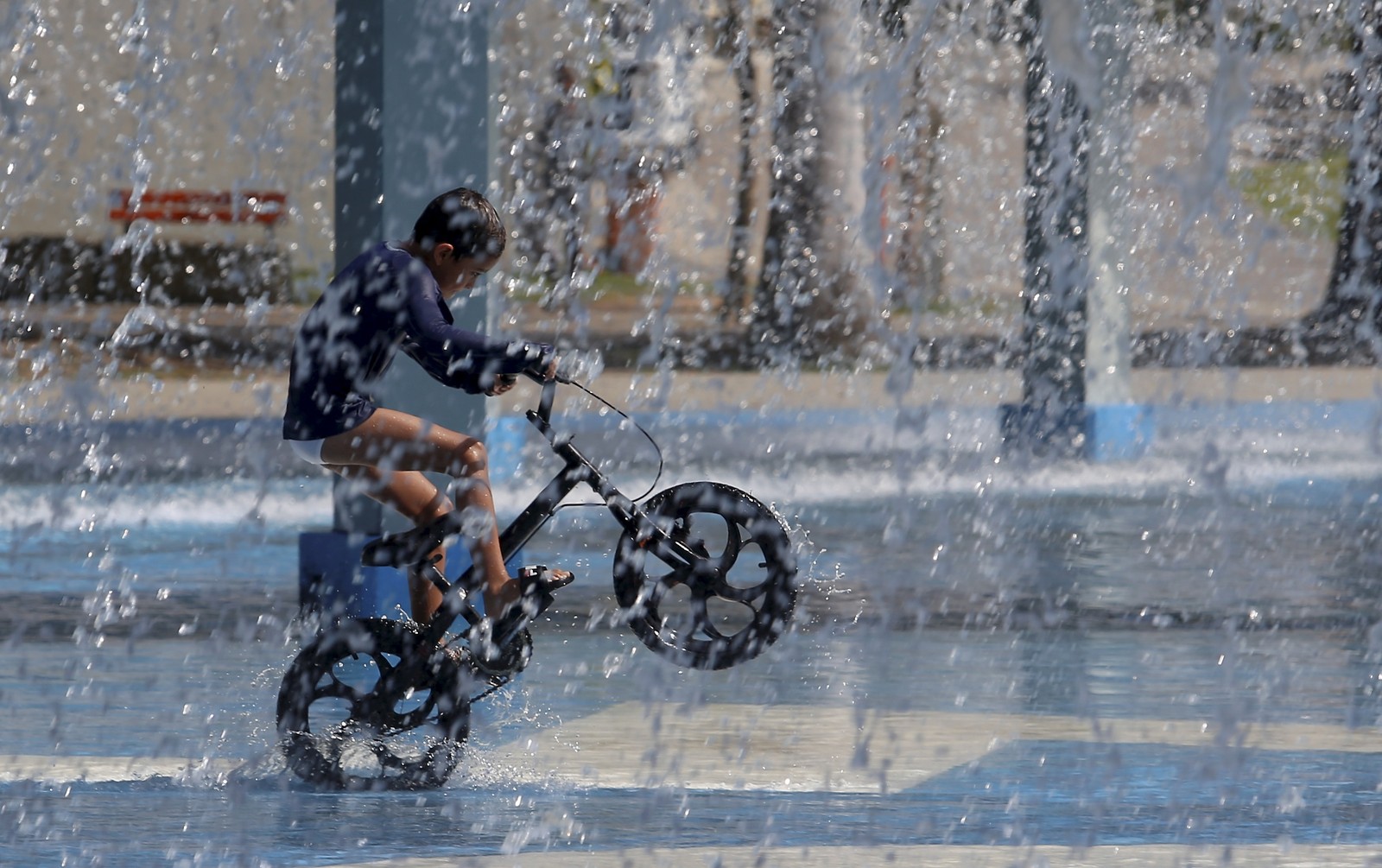Inverno de calor recorde. No Parque de Madureira, um garoto anda de bicicleta embaixo d'água — Foto: Fabiano Rocha